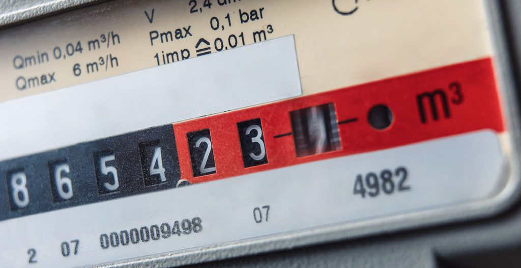Un technicien en bleu de travail note des relevés sur un carnet devant un compteur gaz dans un local technique industriel